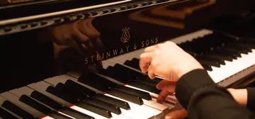 Uma mão toca um piano bem de perto. 