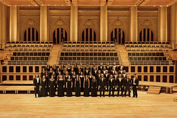 The musicians of the choir are positioned on stage, all dressed in black and smiling.