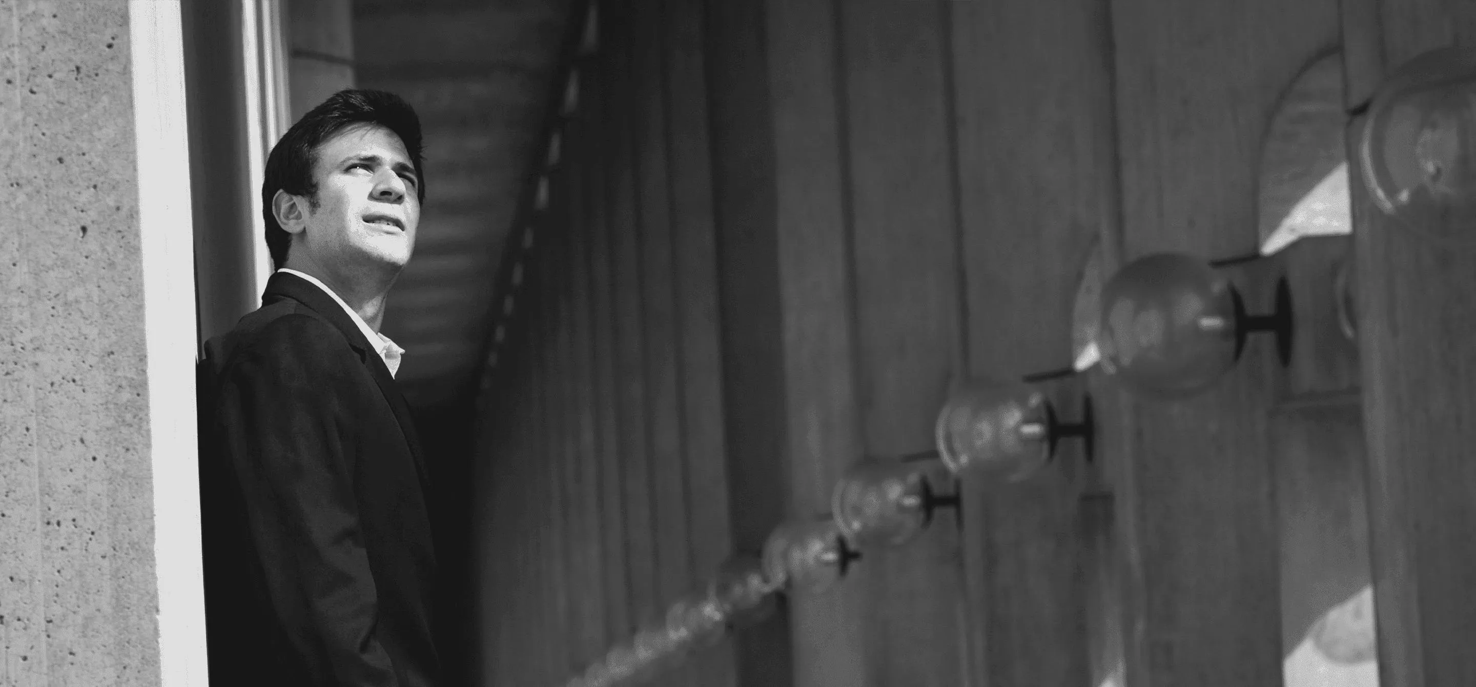 Foto em preto e branco. Pianista Cristian está de pé, encostado em uma parede, com olhar contemplativo.