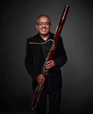 José Arion Linarez is a gray-haired man with glasses. He is wearing a black shirt and holding a bassoon.