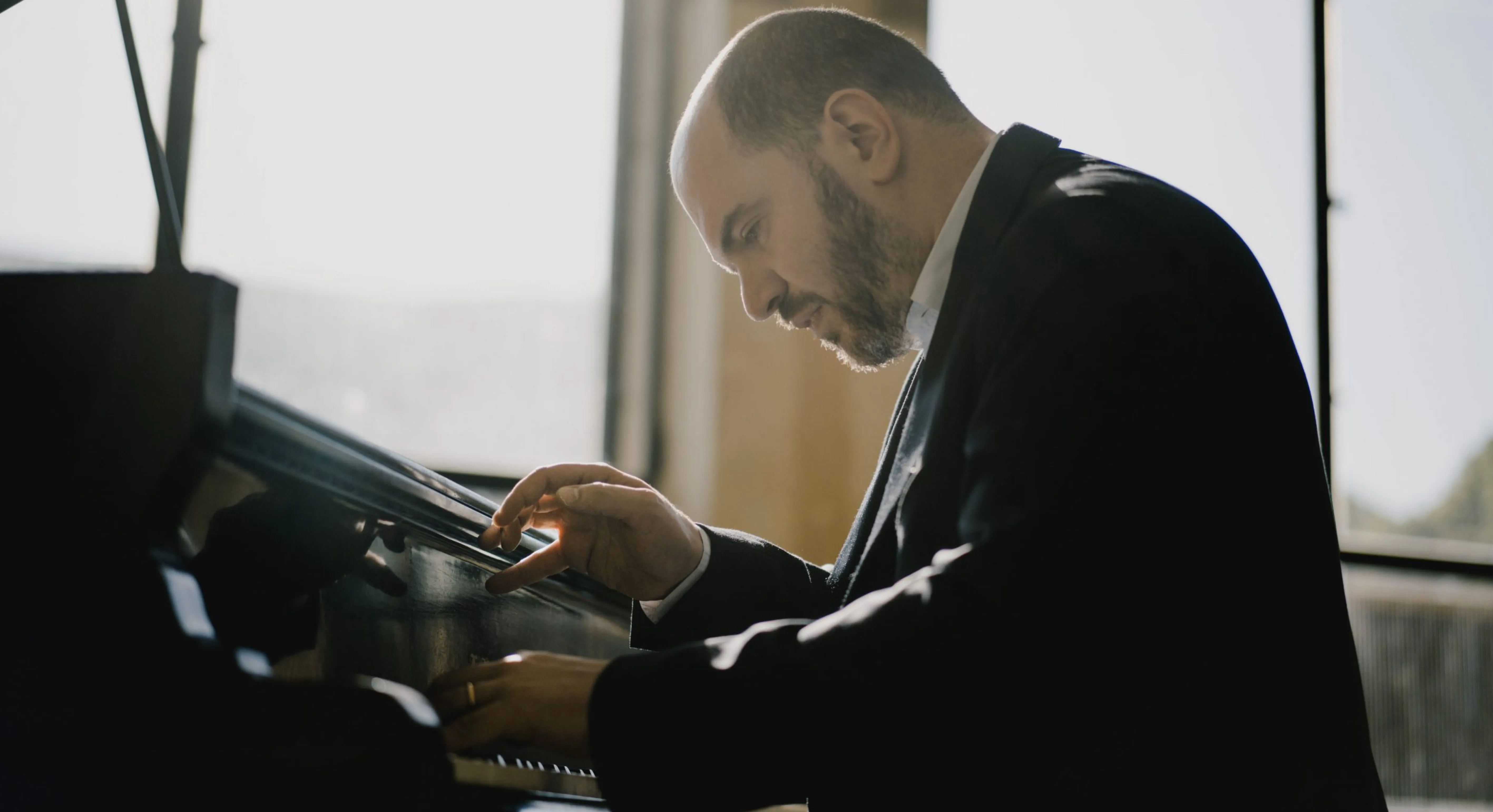 Kirill Gerstein é um homem branco, careca, de terno. Ele está tocando piano.