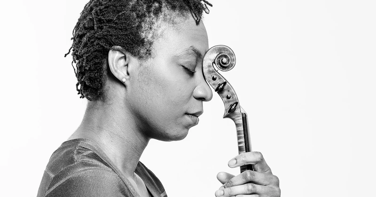 Tai Murray é uma mulher negra de cabelos curtos. Ela está com o rosto encostado no violino, de forma reflexiva.