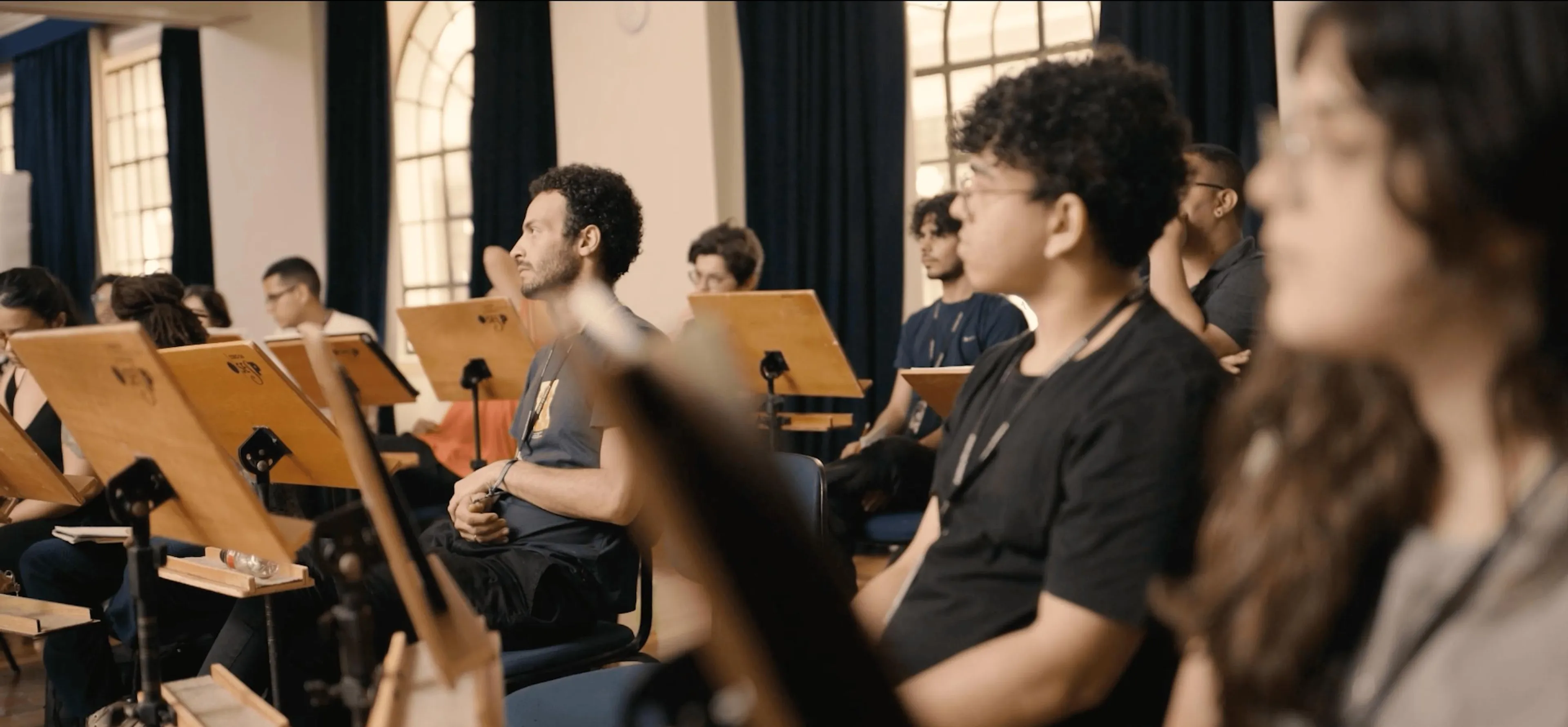 Os alunos da Academia de Música estão assistindo a uma aula sentados.