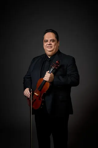 Davi Graton is a white man with brown hair. He is wearing a black shirt and jacket, and he is holding a violin.