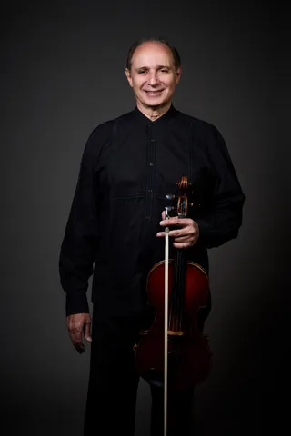 Horácio Schaefer is a bald white man. He is wearing a black shirt and suit jacket, and he is holding a viola.