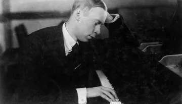 Imagem de Sergei Prokofiev, ele está sentado e apoia a testa na mão esquerda.
