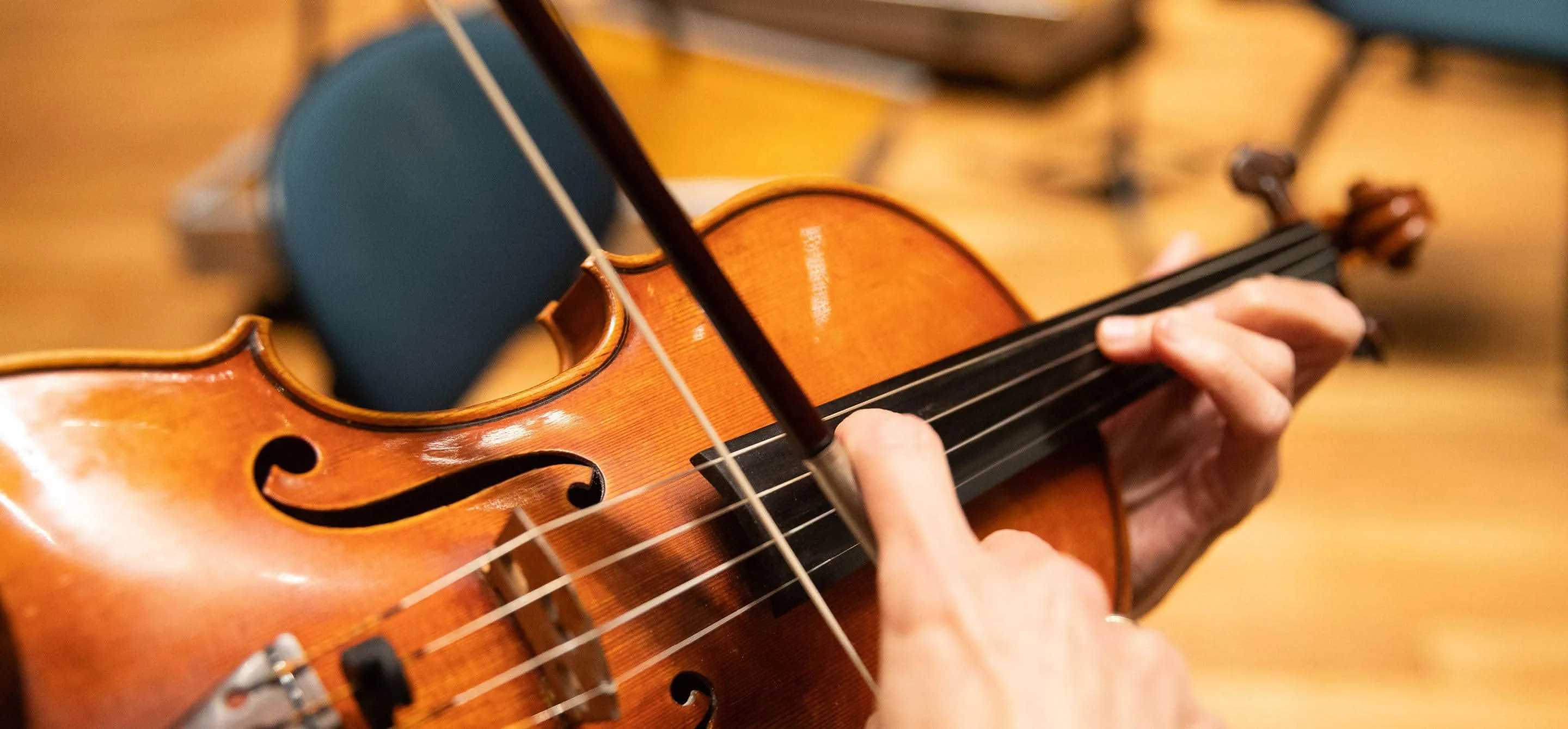 A imagem mostra um violino muito de perto, com destaque para o arco encostando nas cordas.
