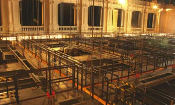 A imagem mostra o forro do teto da Sala São Paulo. É possível ver os cabos que sustentam as placas e o espaço de trabalho acoplado em cima de cada estrutura.
