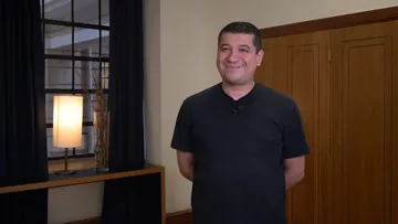 Foto de Pacho Flores, homem branco, de cabelos curtos e escuros. Ele veste camiseta preta e sorri para foto.