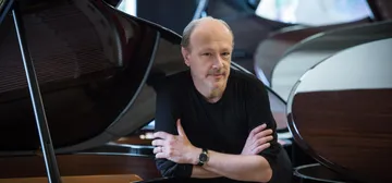 Marc-André Hamelin é um homem branco, calvo e de barba. Ele sorri e usa roupa preta.