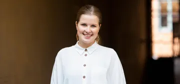 Emilia Hoving é uma mulher branca, loira de cabelos presos. Ela veste camisa branca e sorri.