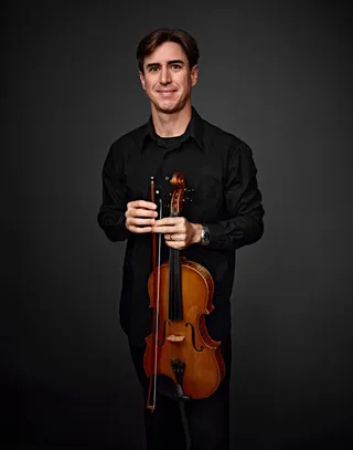 Andrés Lepage is a white man with straight hair and brown eyes. He is wearing a black suit jacket and holding a viola.
