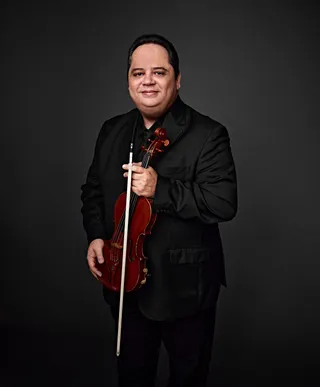 Davi Graton is a white man with brown hair. He is wearing a black shirt and jacket, and he is holding a violin.