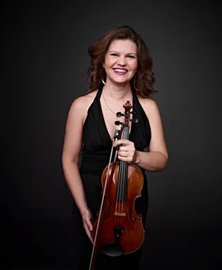Svetlana é uma mulher branca, com cabelo loiro de comprimento médio. Ela tem olhos claros e está usando um vestido preto.